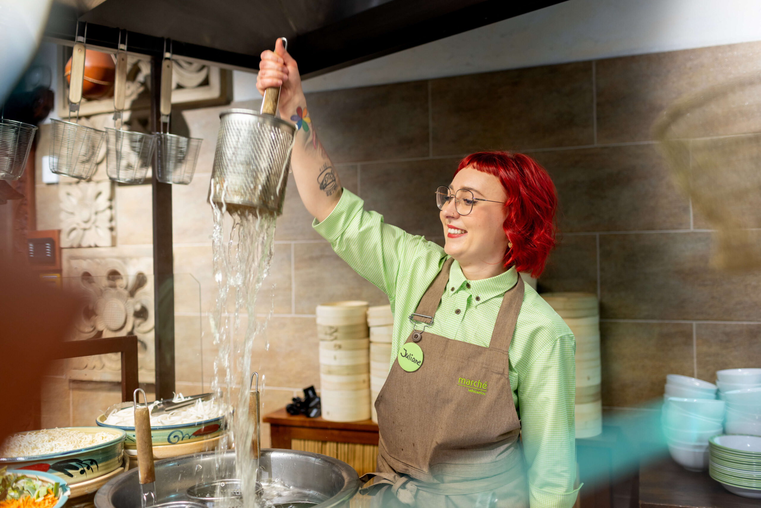 Mitarbeiterin mit einem Nudelsieb am asiatischen Counter